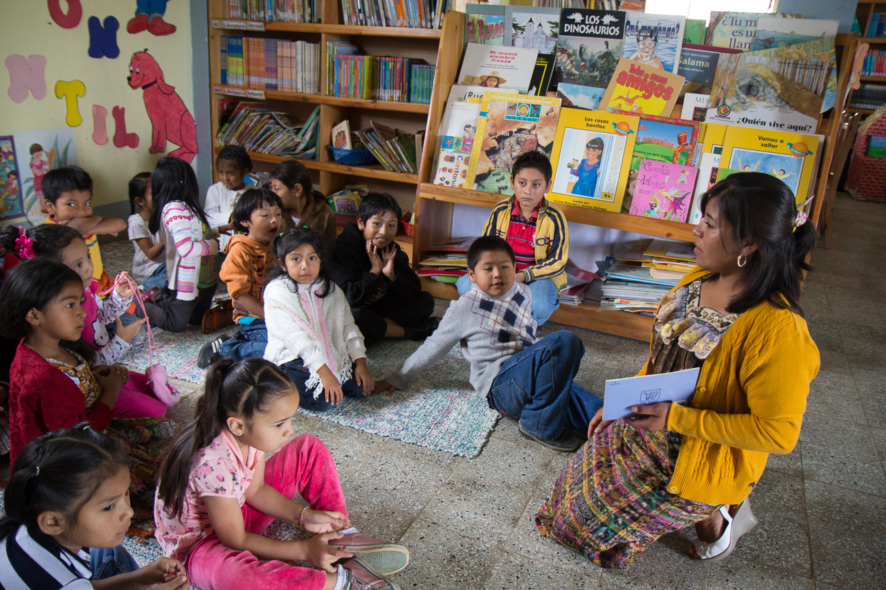 Literacy Trainer Marielena Ixel reads to a group of students at the Melotto School library in El Tejar.